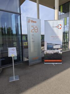 Eingang des Fakultätsgebäudes am Sanderheinrichsleitenweg mit einem IWInet-Aufsteller und einem Wegweiser zur Pratikumsbörse